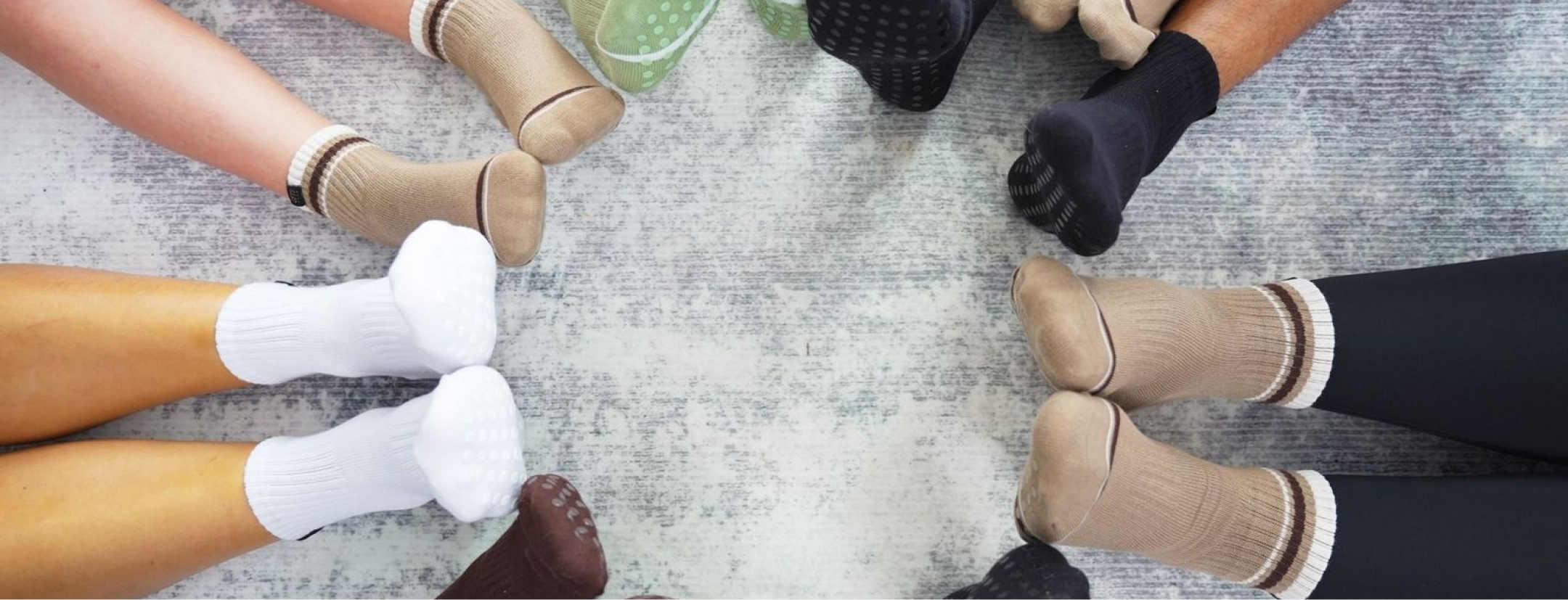 Multiple pairs of feet wearing different colored socks and shoes arranged in a circle on a textured surface.