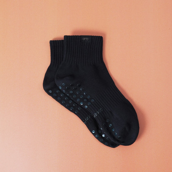 Black ankle sock with grip dots on a peach background