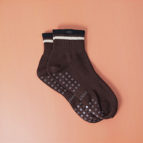 Pair of brown socks with grip dots on a peach background
