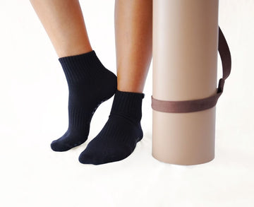 Person wearing black socks with a beige yoga mat and strap on a white background
