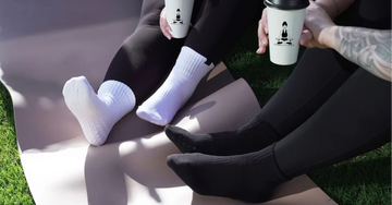 Two people sitting on grass wearing white and black socks with a visible brand logo.