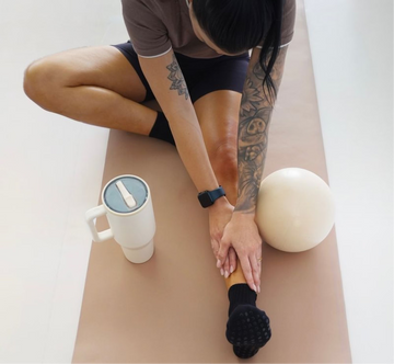 Person stretching on a yoga mat with a mug and ball on the mat
