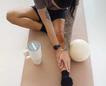 Person stretching on a yoga mat with a mug and ball on the side