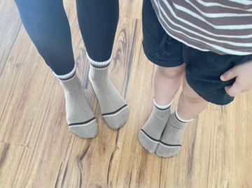 Two pairs of feet wearing gray socks with black accents on a wooden floor.