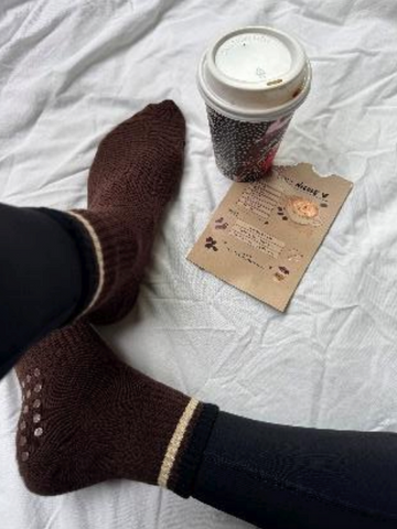 Brown socks on feet with a coffee cup and card on a white surface