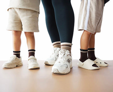 Three pairs of legs wearing sneakers on a plain background