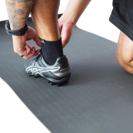 Person putting on a soccer cleat on a gray mat
