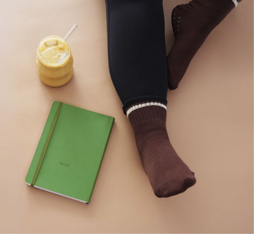 Green notebook, lemonade, and legs with socks on a beige surface